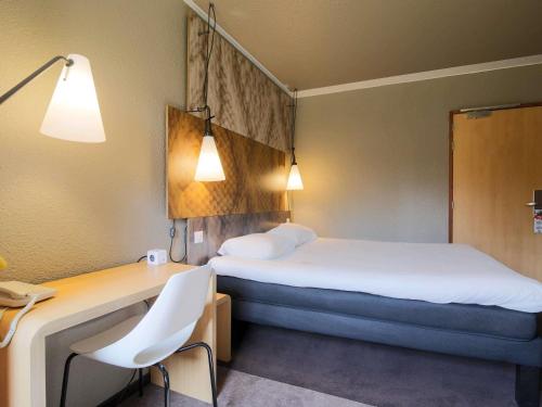a hotel room with a bed and a desk with a chair at ibis Montauban in Montauban