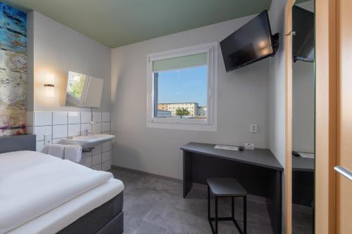 a hotel room with a bed and a desk and a tv at Felix Hotel Darmstadt in Darmstadt