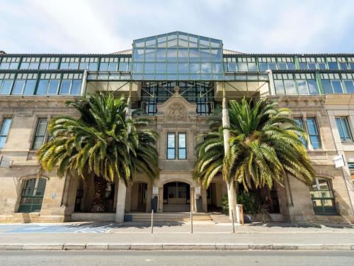 a building with two palm trees in front of it at Mercure Bordeaux Chateau Chartrons in Bordeaux