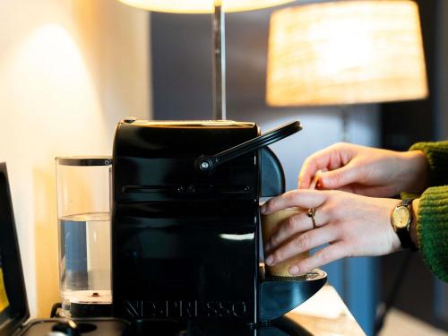 a woman is taking a drink from a coffee machine at Mercure Bordeaux Chateau Chartrons in Bordeaux