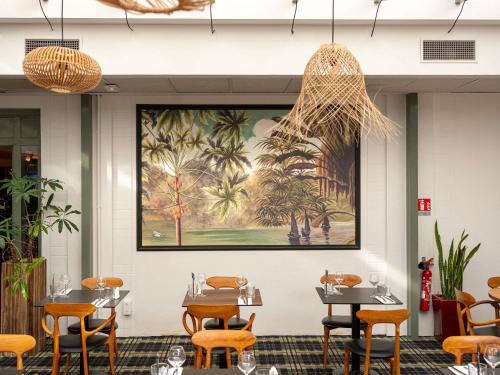 a restaurant with tables and chairs and a painting of palm trees at Mercure Bordeaux Chateau Chartrons in Bordeaux