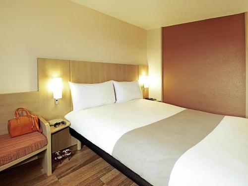 a hotel room with a large white bed and a red purse at ibis Koblenz City in Koblenz