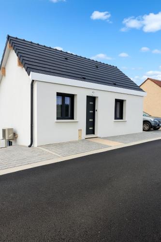 a white house with a black roof on a street at Maison individuelle meublée in Chaignay