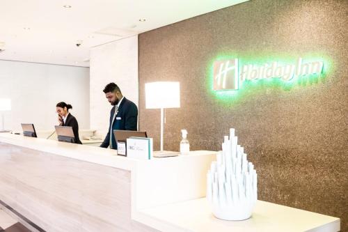 two men standing at a reception desk with their laptops at Holiday Inn Mauritius Mon Trésor by IHG in Blue Bay