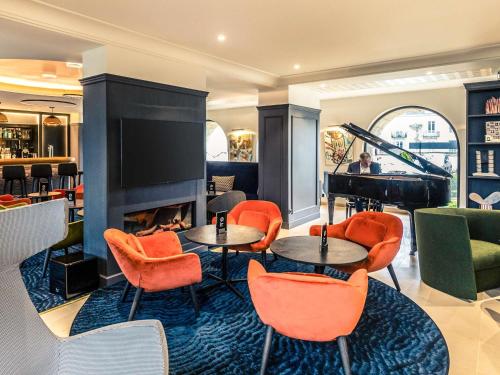 a lobby with tables and chairs and a piano at Hotel De Bourbon Grand Hotel Mercure Bourges in Bourges