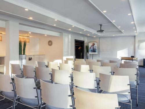 an empty room with white chairs and a podium at Novotel Luxembourg Kirchberg in Luxembourg