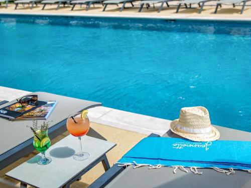 a table with a hat and a drink next to a swimming pool at Mercure Cavaillon in Cavaillon