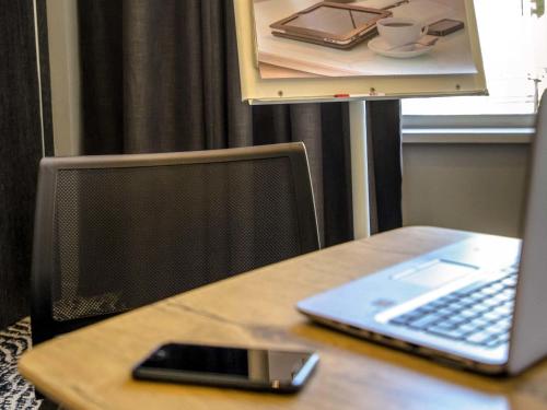 a desk with a laptop and a cell phone on it at Mercure Cavaillon in Cavaillon