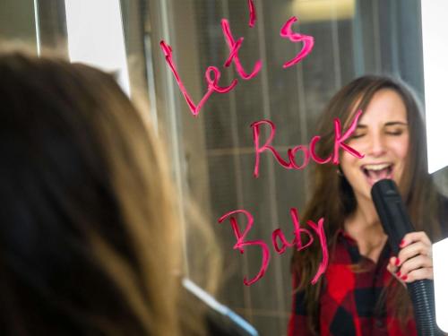 a woman singing into a microphone in front of a mirror at ibis Paris Gennevilliers in Gennevilliers