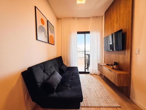 a living room with a black couch and a television at Apto com 1 quarto e sacada com churrasqueira in Brusque