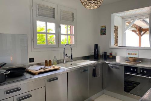 a white kitchen with a sink and two windows at Villa Le Nid des Colibris in Saint-Charles