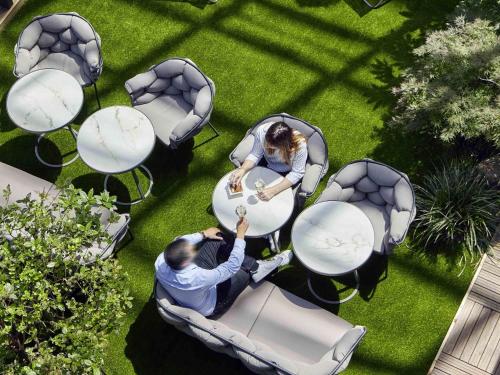 a man and woman sitting at a table in a garden at Mercure Paris la Défense Grande Arche in Nanterre