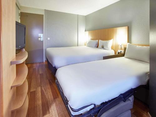 a hotel room with two beds and a flat screen tv at ibis Haguenau Strasbourg Nord in Haguenau