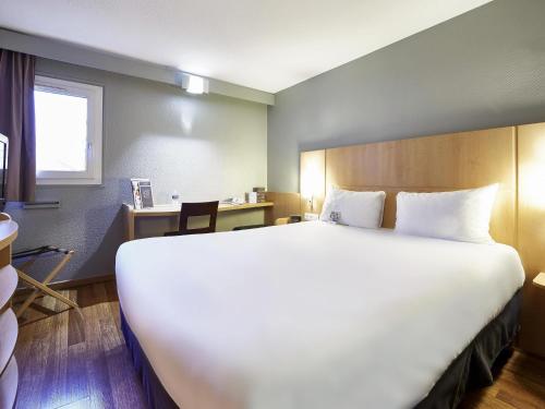 a large white bed in a room with a desk at ibis Haguenau Strasbourg Nord in Haguenau