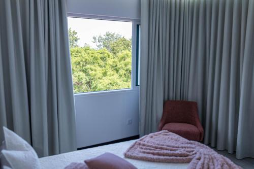 a bedroom with a bed and a chair and a window at MCM Matur Flats 2, 11 Duplex in Santa Cruz