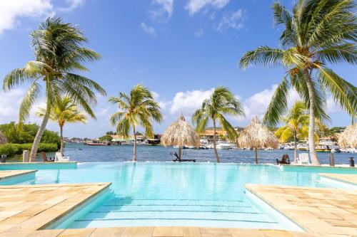 a swimming pool with palm trees and a body of water at Tropical Escape with Pool and Ocean Views in Willemstad