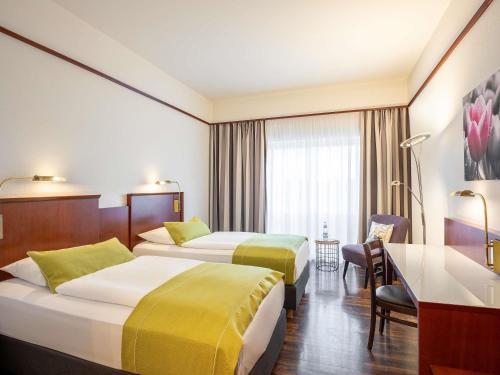 a hotel room with two beds and a desk at Mercure Hotel Bad Oeynhausen City in Bad Oeynhausen