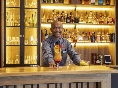 a man standing behind a bar with a drink at Mercure Hotel Bad Oeynhausen City in Bad Oeynhausen