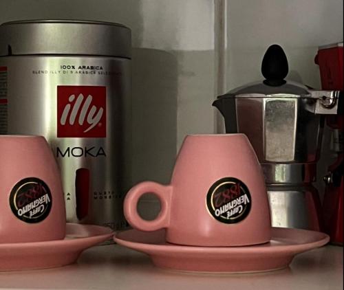 two pink mugs sitting on plates next to a coffee pot at Appartamento CasaZeta luminoso e centralissimo in Latina