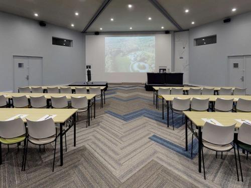 a room with tables and chairs and a projection screen at ibis Styles Louvain-la-Neuve Hotel and Events in Louvain-la-Neuve
