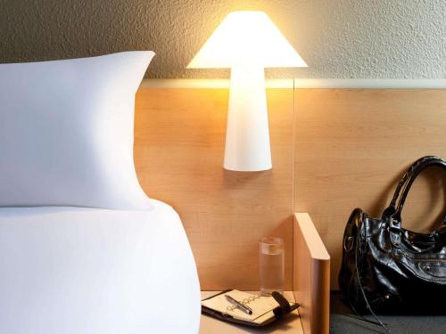 a bedroom with a bed with a lamp and a black purse at ibis Luebeck City in Lübeck