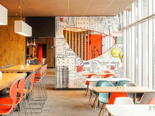a restaurant with tables and chairs and a wall with drawings at ibis Luebeck City in Lübeck