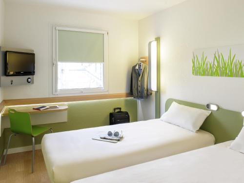 a room with two beds and a desk and a tv at ibis budget Nürnberg City Messe in Nürnberg