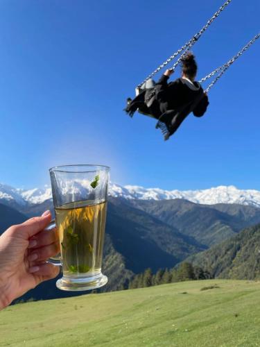 a person is holding a glass of tea on a swing at Heshkili huts and cabins Svaneti in Keshkili