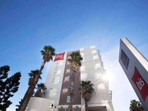 a hotel with palm trees in front of a building at ibis Sydney Olympic Park in Sydney