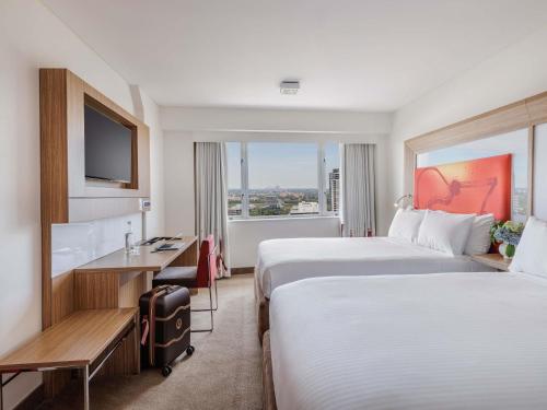 a hotel room with two beds and a desk and a window at Novotel Sydney Olympic Park in Sydney