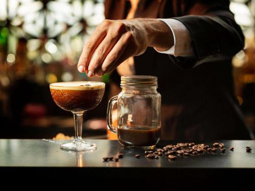 a person is stirring a drink next to a glass at Novotel Sydney Olympic Park in Sydney