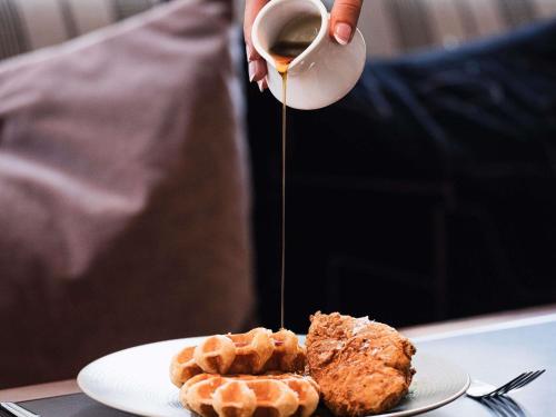 a person holding a cup of coffee next to a plate of waffles at Sofitel Philadelphia at Rittenhouse Square in Philadelphia
