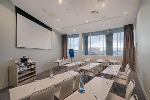 a conference room with tables and chairs and a projection screen at NH Toulouse Airport in Blagnac