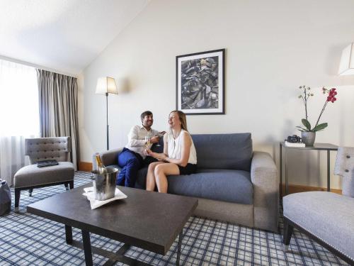 a man and woman sitting on a couch in a hotel room at Mercure Luxembourg Kikuoka Golf & Spa in Canach