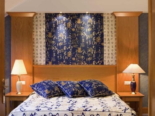 a bedroom with a bed with blue pillows and a wall at Mercure Luxembourg Kikuoka Golf & Spa in Canach