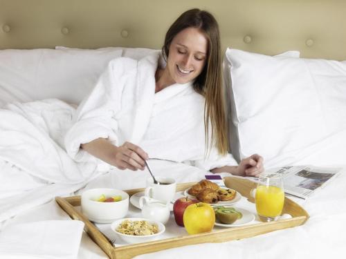 a woman sitting in bed with a tray of food at Mercure Luxembourg Kikuoka Golf & Spa in Canach