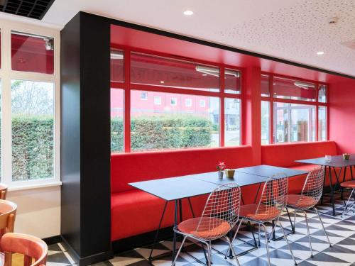 a restaurant with red walls and tables and chairs at ibis Strasbourg Sud La Vigie in Ostwald