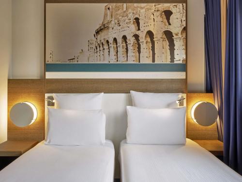 two beds in a hotel room with a picture of the coliseum at Mercure Roma Centro Colosseo in Rome