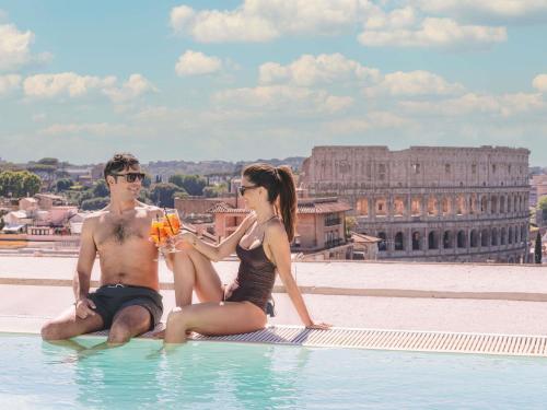 a man and woman sitting on the edge of a swimming pool at Mercure Roma Centro Colosseo in Rome