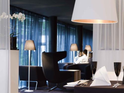 a living room with a chair and people sitting in a room at Congress Hotel Mercure Nürnberg an der Messe in Nürnberg