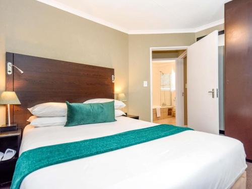 a bedroom with a large white bed with a green pillow at Mercure Hotel Bedfordview in Johannesburg