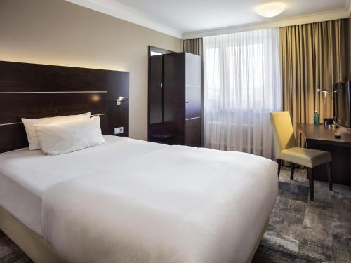a hotel room with a large white bed and a desk at Mercure Hotel Hagen in Hagen