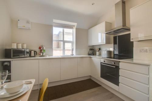 a kitchen with white cabinets and a table and a window at Cyril’s - Ellinbrook Apartments in Hunstanton