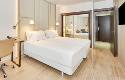 a bedroom with a large white bed and a desk at NH Imperial Playa in Las Palmas de Gran Canaria