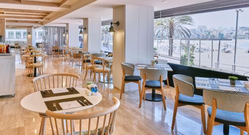 a restaurant with tables and chairs and a large window at NH Imperial Playa in Las Palmas de Gran Canaria