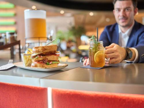 a man sitting at a table with a sandwich and a drink at ibis Zürich City West in Zürich