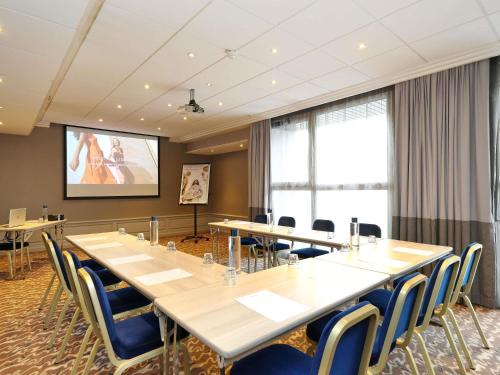 a conference room with tables and chairs and a projection screen at Mercure Grenoble Centre Porte des Alpes in Grenoble