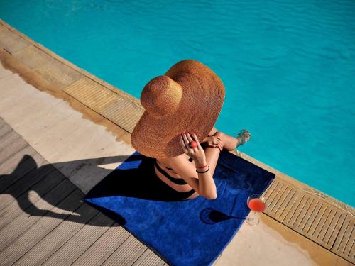 a person wearing a hat sitting next to a pool at Le Médina Essaouira Thalassa Sea & Spa - MGallery Collection in Essaouira