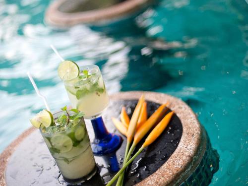 two drinks on a tray next to a swimming pool at Sofitel Angkor Phokeethra Golf & Spa Resort in Siem Reap