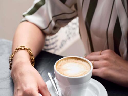 a woman sitting at a table with a cup of coffee at Sofitel Athens Airport in Athens